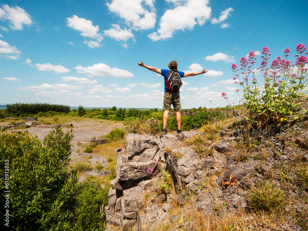 Slim athletic man on edge of a cliff hands up in the air, beautiful nature scene on a warm sunny day. Outdoor activity. Get out of town and adventure concept. Blue cloudy sky. Be active theme