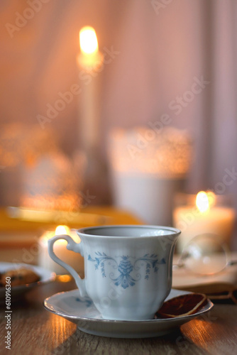 Cup of tea or coffee, plate of cookies, books, e-reader, pencil and lit candles on the table. Selective focus.