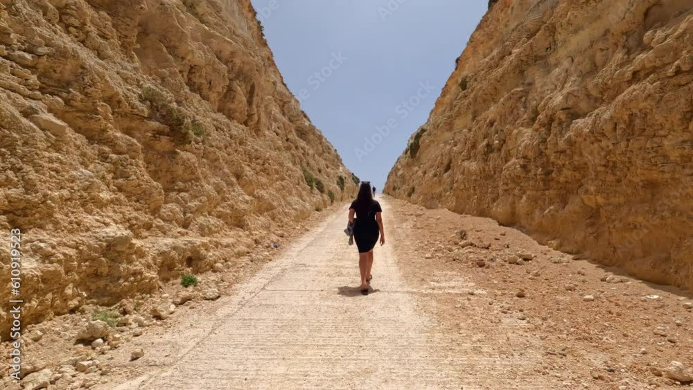 Young woman walking along a trail in a steep canyon between cliffs Young woman walking along a trail in a steep canyon between cliffs