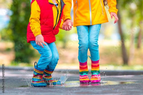 Happy kids girl and boy with umbrella and colorful rubber rain boots playing outdoor and jumping in rainy puddle