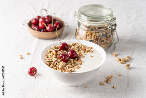 Bowl of homemade granola with nuts and cherry in white bowl on light background. Quick healthy breakfast