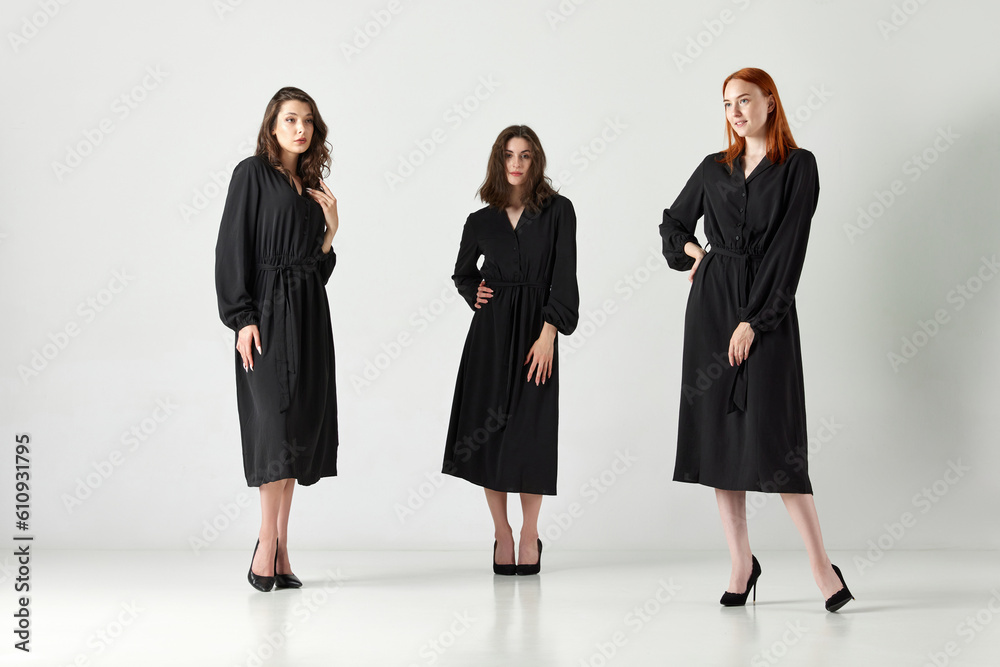 Portrait of three stylihs, beautiful young women in elegant black dresses posing against light studio background. Concept of elegant fashion, female beauty, business, shopping, sales, ad Portrait of three stylihs, beautiful young women in elegant black dresses posing against light studio background. Concept of elegant fashion, female beauty, business, shopping, sales, ad