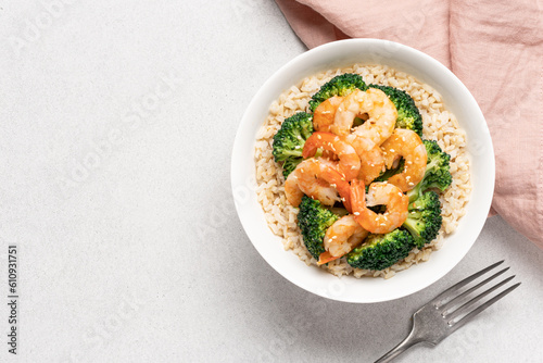 Rice with broccoli and fried shrimp in white bowl on light background with copy space. Healthy food with vegetables and seafood