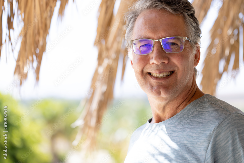 Portrait of caucasian smiling senior man wearing eyeglasses standing at tourist resort in summer