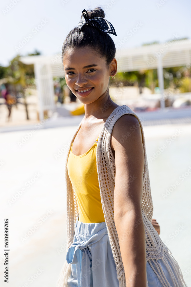 Portrait of caucasian stylish young woman standing at tourist resort at beach against clear sky