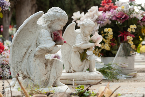 Vista de dos angelitos arrodillados sosteniendo flores orando por algún difunto.