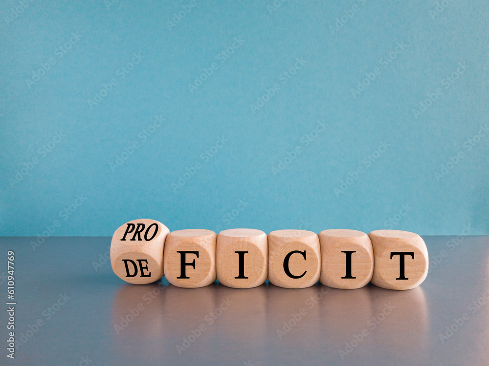 Proficit or deficit symbol. Turned wooden cube and changes the concept word deficit to proficit. Beautiful light blue background. Business proficit or deficit concept. Copy space. - obrazy, fototapety, plakaty 