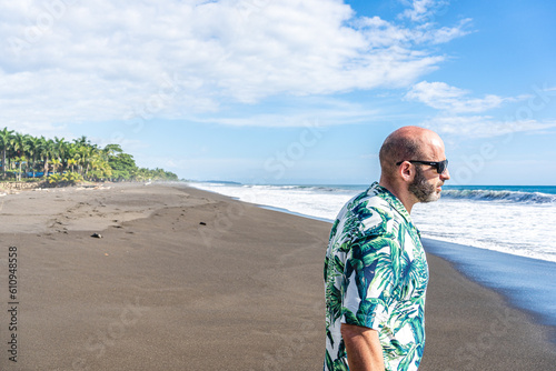 Man with a Hawaiian shirt walking along a tropical beach