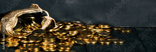 A bag with gold coins on a wooden background banner. The money is in a black bag. Treasure Hunt. A Purse with money on a black background. Wallet wit gold coins. photo