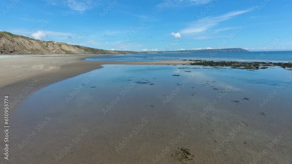 Low altitude aerial flight of sandy beach with shoal of fish in shallow waters against a backdrop of sandy cliffs and blue summer skies at Hell`s Mouth in North Wales. Low altitude aerial flight of sandy beach with shoal of fish in shallow waters against a backdrop of sandy cliffs and blue summer skies at Hell`s Mouth in North Wales.