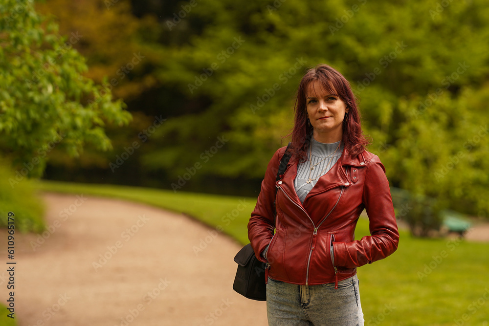 Young fashion woman walking in city park. Stylish female model in leather jacket.