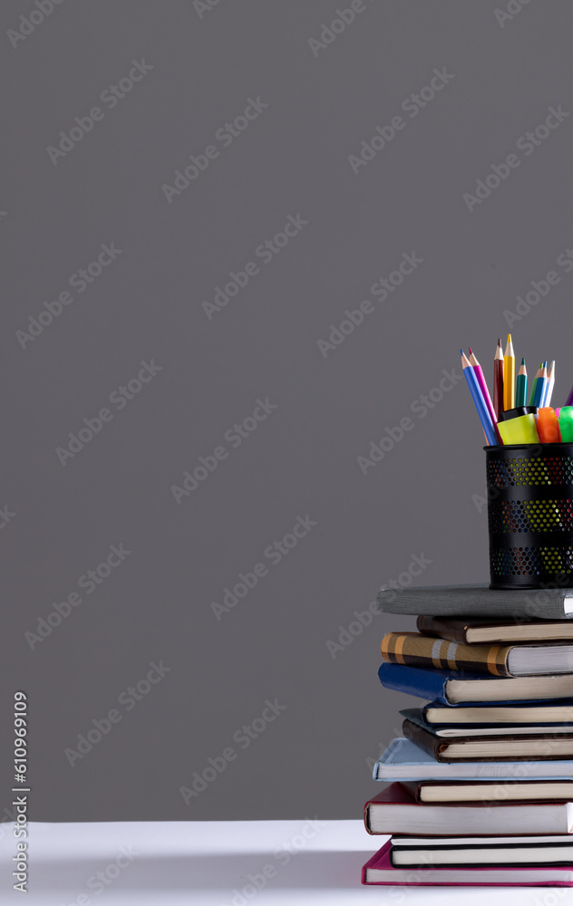 Fototapeta premium Stack of books and notebooks with pencil container on top and copy space on grey background