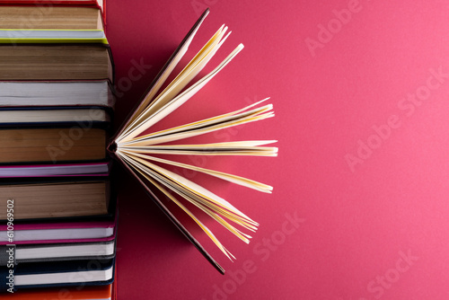 Books and notebooks in row with opened notebook on top and copy space on red background