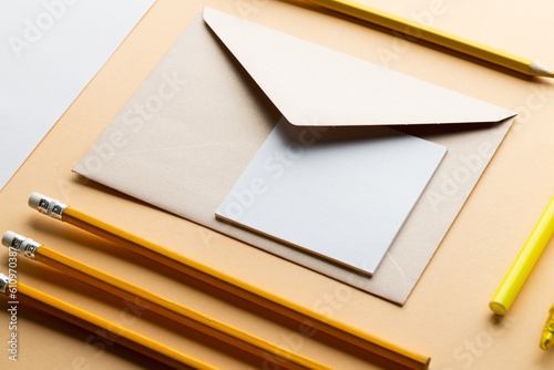 Flat lay of yellow pencils and marker, envelope and white paper with copy space on yellow background