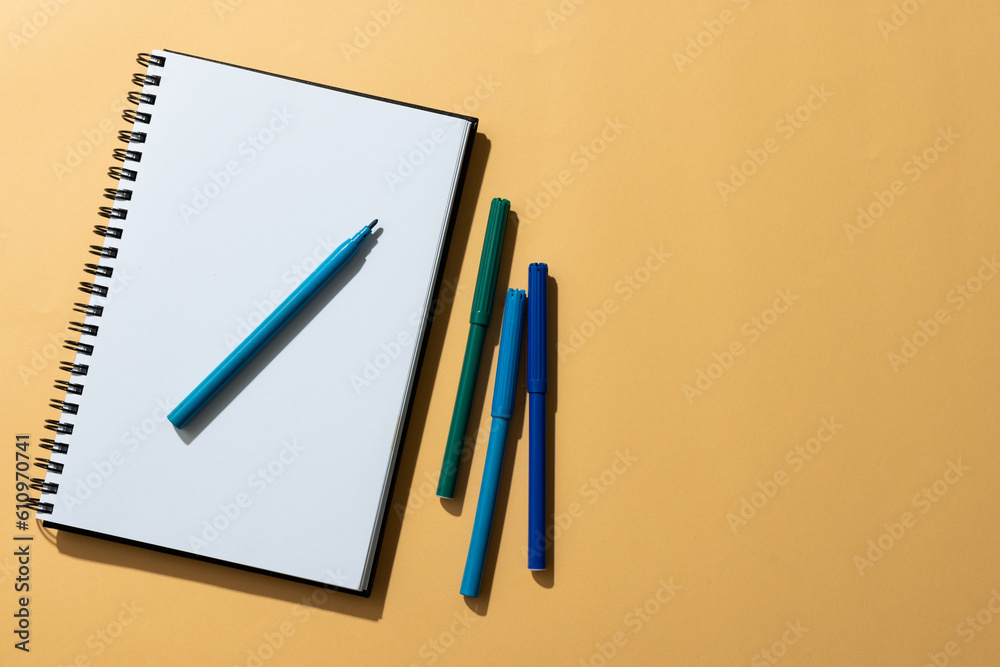 Close up of notebook and four markers with copy space on orange background Close up of notebook and four markers with copy space on orange background
