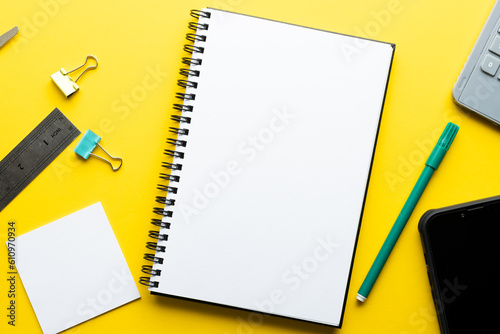 Flat lay of notebook with copy space and writing materials on yellow background