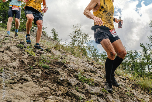 group athletes runners running down steep mountainside, summer trail marathon race