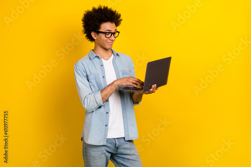 Photo of cheerful funny man wear jeans shirt spectacles working modern gadget smiling isolated yellow color background