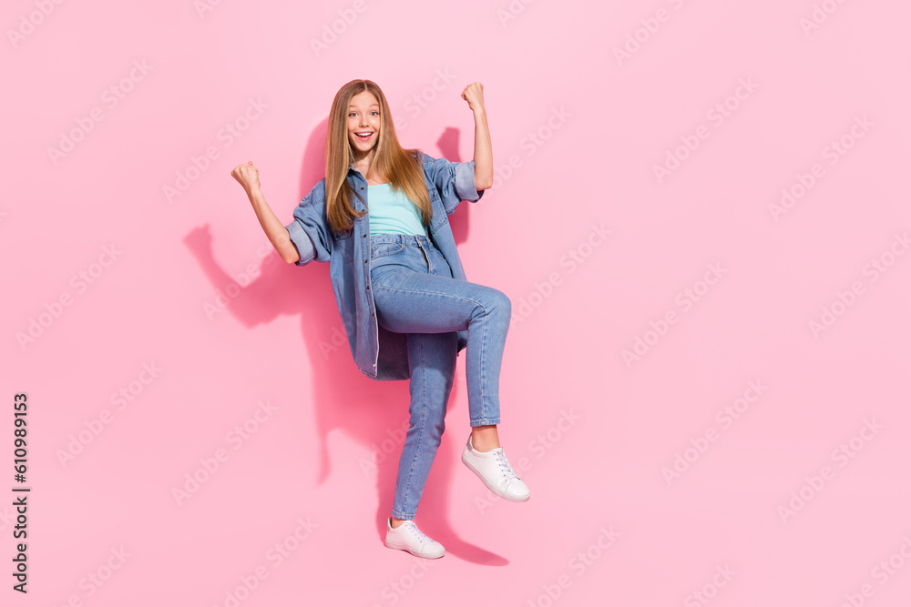 Full body photo of pretty young teenager girl raise fists celebrate lottery wear trendy jeans outfit isolated on pink color background Full body photo of pretty young teenager girl raise fists celebrate lottery wear trendy jeans outfit isolated on pink color background