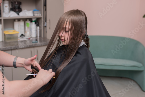 a happy child cuts her hair in a beauty salon or a barber shop. children's haircut in a beauty salon, a female hairdresser cuts a girl with scissors.