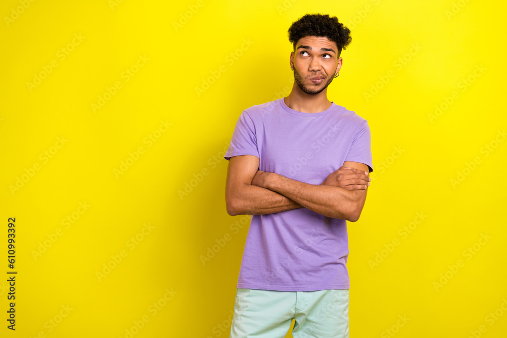 Photo of doubtful unsure man wear violet t-shirt arms crossed looking empty space isolated yellow color background
