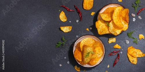 Photography Bowls of homemade potato chips served with chili, parsley, seal salt on black st