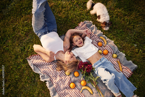 On the blanket with oranges and bananas. Woman with her little daughter are on the summer field together