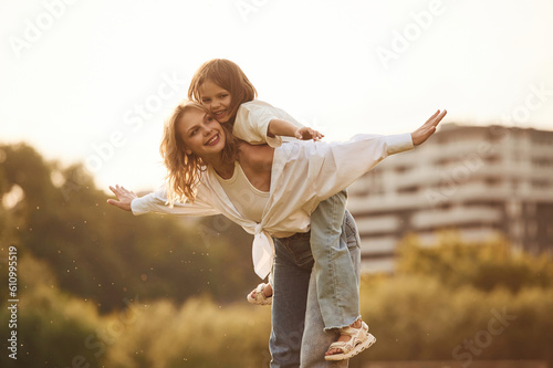 Sitting on the mother shoulders. Woman with her little daughter are on the summer field together