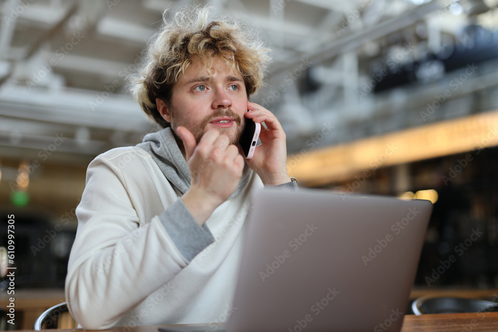 Curly bearded male freelancer talking on the phone while working on a laptop. Curly bearded male freelancer talking on the phone while working on a laptop.