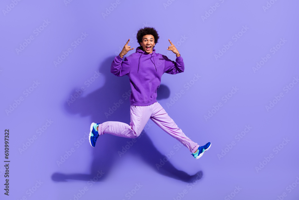 Full size photo of positive crazy person wear stylish pullover jumping showing horns rock symbol isolated on purple color background Full size photo of positive crazy person wear stylish pullover jumping showing horns rock symbol isolated on purple color background