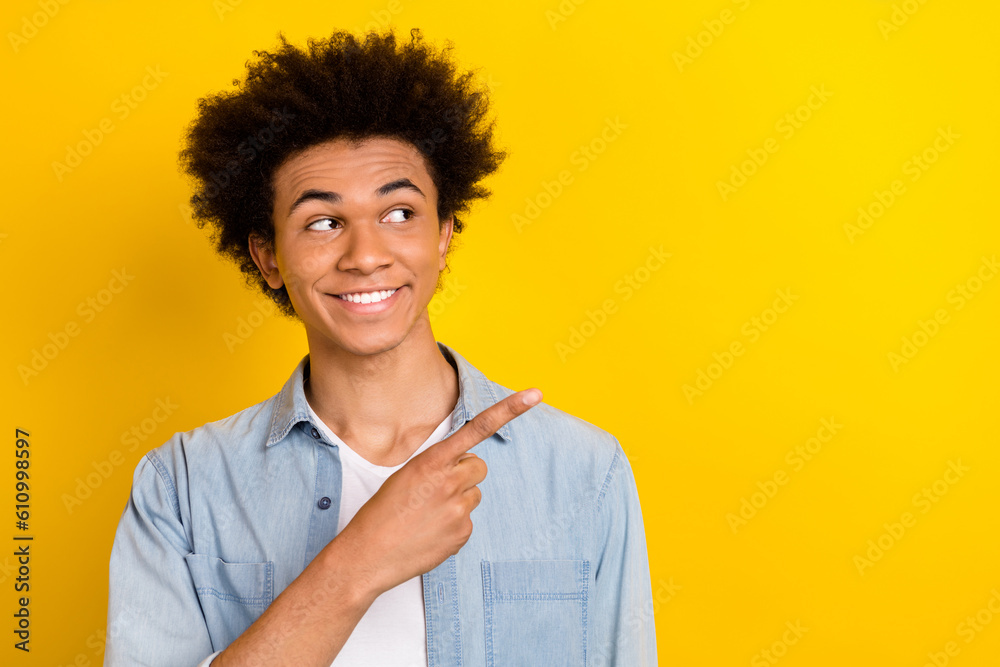 Photo of toothy beaming guy dressed denim shirt looking showing finger empty space isolated yellow color background Photo of toothy beaming guy dressed denim shirt looking showing finger empty space isolated yellow color background