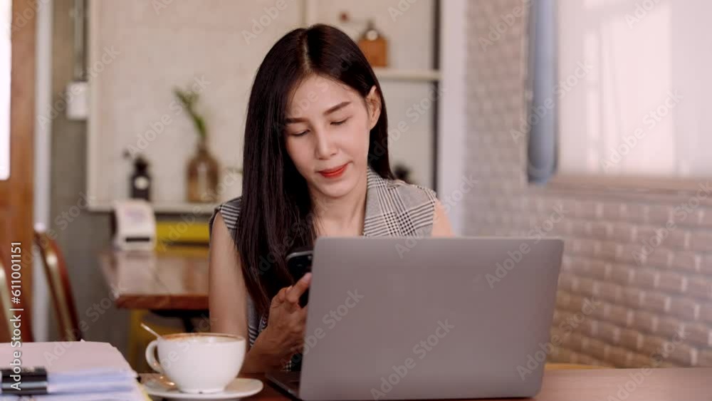 Close-up young Asian woman sitting on mobile phone, while resting eyes from work, looked at laptop screen on desk in front expression looked cheerful happy, as typed read text on the screen. Close-up young Asian woman sitting on mobile phone, while resting eyes from work, looked at laptop screen on desk in front expression looked cheerful happy, as typed read text on the screen.