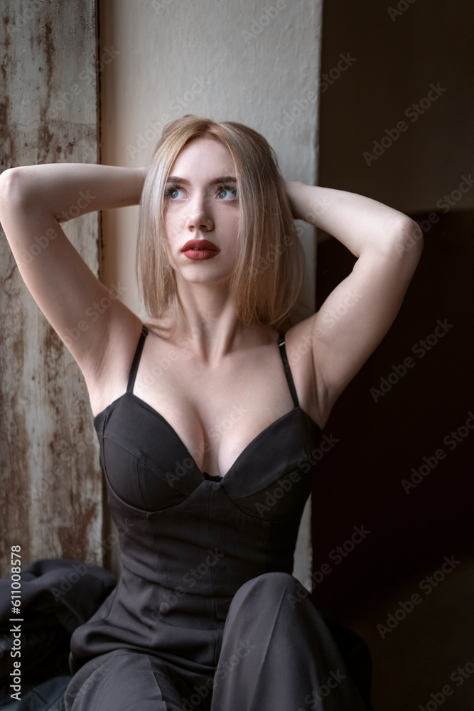 Attractive young blonde woman wears black top with deep sweetheart neckline with her hands behind head. Girl with seductive figure. Attractive young blonde woman wears black top with deep sweetheart neckline with her hands behind head. Girl with seductive figure.