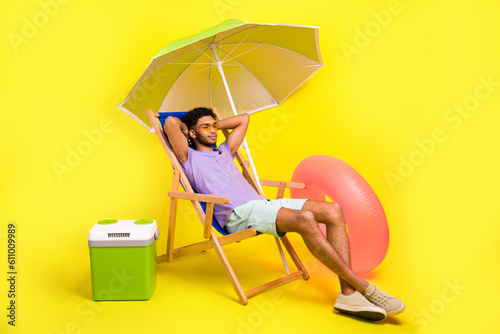 Full length cadre of funny guy wear sunglass sunbed under parasol near beer fridge will swim rubber ring isolated on yellow color background
