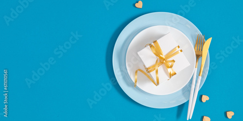 Father's Day concept. Flat lay top view of plate, gift box, cutlery, knife, fork and hearts on blue background with space for text or promotion and greeting message, banner