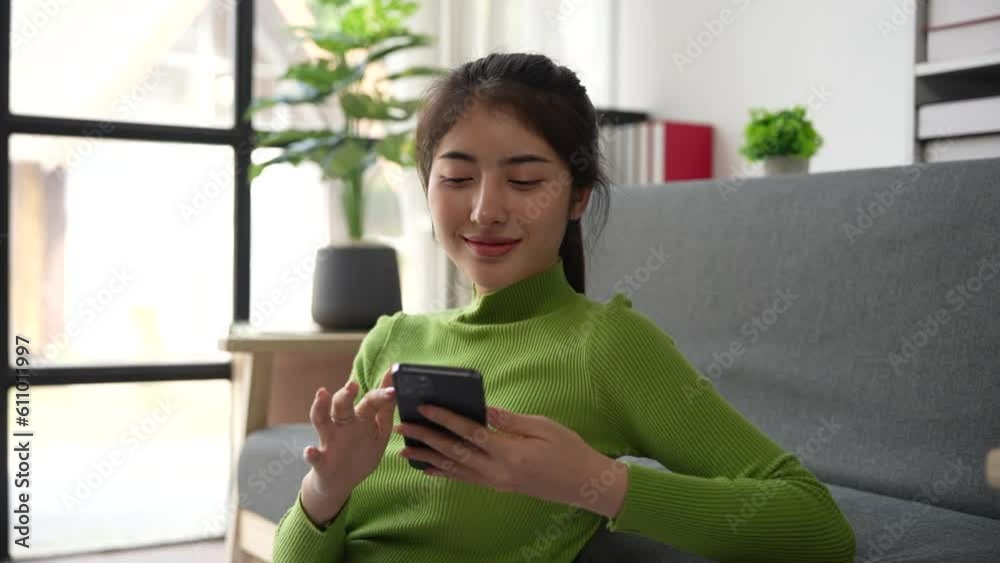 Smiling happy Asian woman typing swipe touchscreen of phone girl cheerful choosing shopping in online e-commerce app female enjoy mobile website play game at home follow post in social media Smiling happy Asian woman typing swipe touchscreen of phone girl cheerful choosing shopping in online e-commerce app female enjoy mobile website play game at home follow post in social media