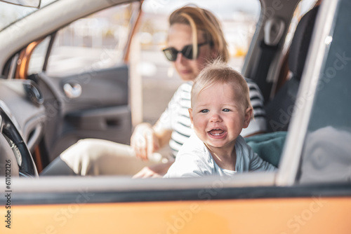 Mother and her infant baby boy child on family summer travel road trip, sitting at dad's front seat, waiting in the car for father to buy farry tickets photo