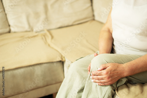 Senior woman suffering from knee pain on a sofa. People, health care and problem concept.