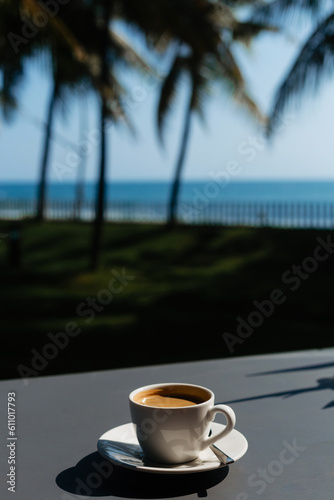 A cup of black coffee against the backdrop of palm trees and the ocean. Rest on the sea at the hotel. Delicious coffee in nature