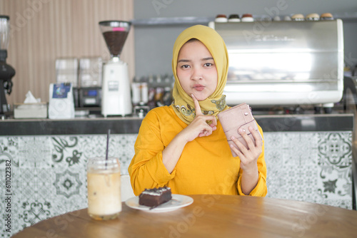 Asian hijab woman wearing Orange T-shirt thinking something wallet