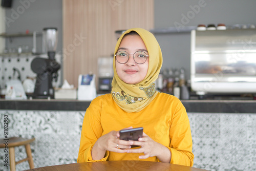 Asian hijab woman wearing Orange T-shirt holding mobile phone