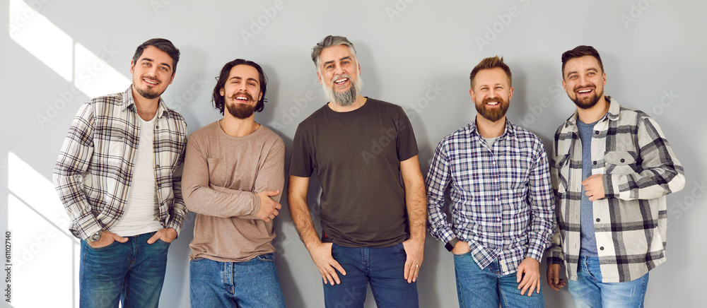 © Studio Romantic - Happy men in casual clothes. Group of cheerful male fashion models of different ages wearing quiet subdued color plain Tshirts or plaid shirts standing by gray background looking at camera and smiling