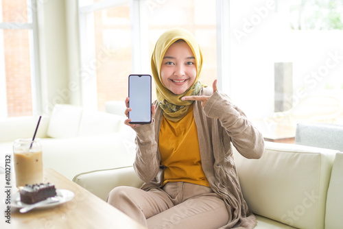business Asian hijab woman wearing Orange T-shirt pointing blank phone