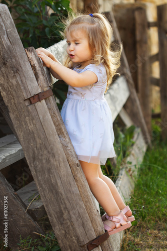 A little girl in a blue dress on a broken fence in the summer