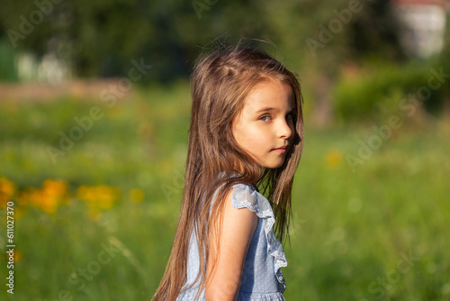 Little beautiful girl in a blue dress barefoot in the summer on the street on a green background