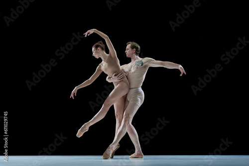 Impressive young man and woman, talented, professional dancers performing ballet art against black studio background. Concept of beauty, classical dance style, inspiration, movements. Ad