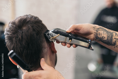 Anonymous young barber cutting hair with machine in hair salon photo