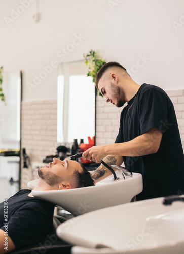 Young barber washing hair in barber shop