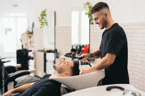 Young barber washing hair in barber shop photo