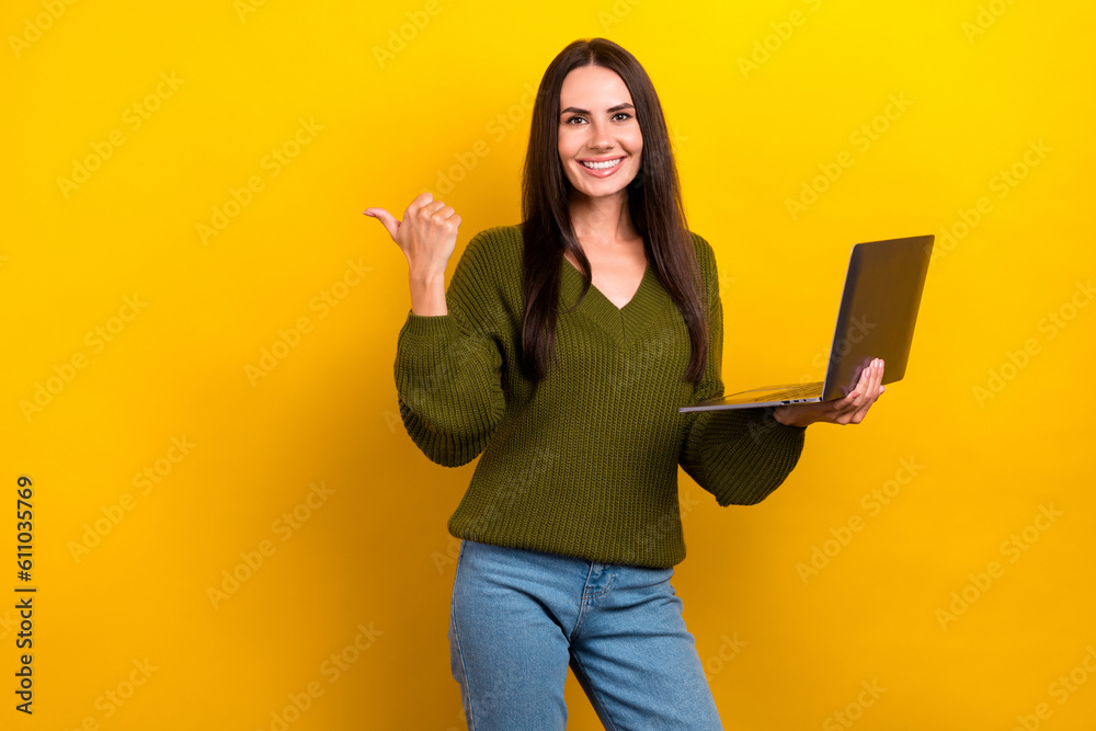 Photo of pretty shiny woman dressed khaki sweater working modern device pointing thumb empty space isolated yellow color background Photo of pretty shiny woman dressed khaki sweater working modern device pointing thumb empty space isolated yellow color background
